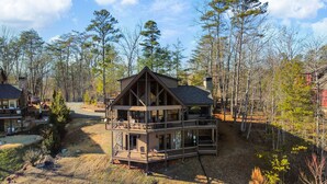 Une cabane dotée d’une grande terrasse, de nombreuses fenêtres et d’une cheminée en pierre.