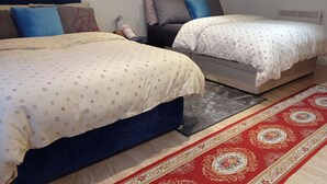 A bedroom with two beds, a red patterned rug, and a grey headboard.