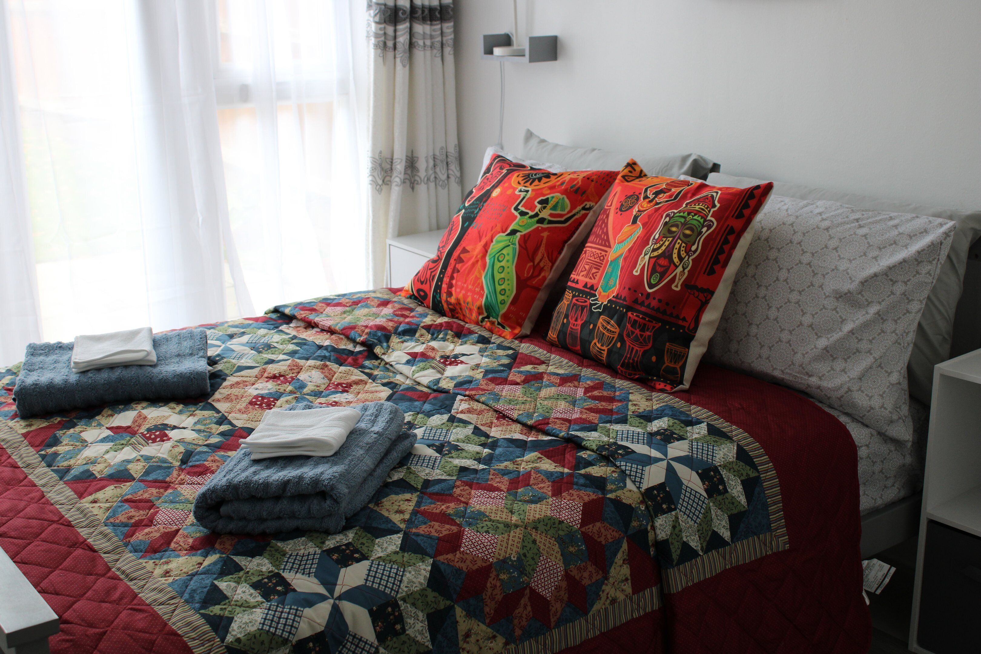 Una cama bien hecha con un edredón colorido, dos almohadas con diseños intrincados y toallas dobladas sobre la cama.