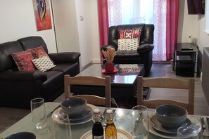 A dining area with a glass table set for two, two black bowls, two wine bottles, and a vase with dried plants. - Apartment - Sleeps 4 - Parking - Station Close (London)