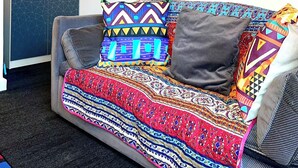 En sofa med et farverigt mønstret tæppe og to puder, hvoraf den ene har et geometrisk design og den anden et stribet mønster.