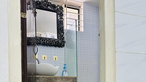 A bathroom with a white sink, a glass mirror, and a pair of black slippers on the floor. - Beautiful 1-Bed Studio in Dhaka (Dhaka)
