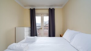 Habitación de hotel con una cama grande, una mesita de noche, un armario y vistas a un balcón con barandilla.