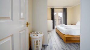 Habitación de hotel con una cama de madera, un cubo de basura blanco y vistas al exterior a través de una ventana con cortinas.