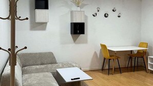Una sala de estar moderna con un sofá gris, una mesa de centro de madera, una mesa de comedor con sillas amarillas y un perchero.
