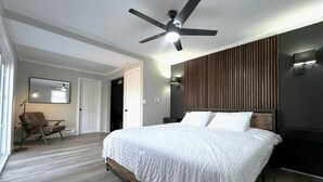 A modern bedroom with a large bed, a ceiling fan, and a wooden panel wall.
