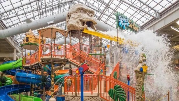 An indoor water park with multiple slides and water features, including a large waterfall and a climbing structure.