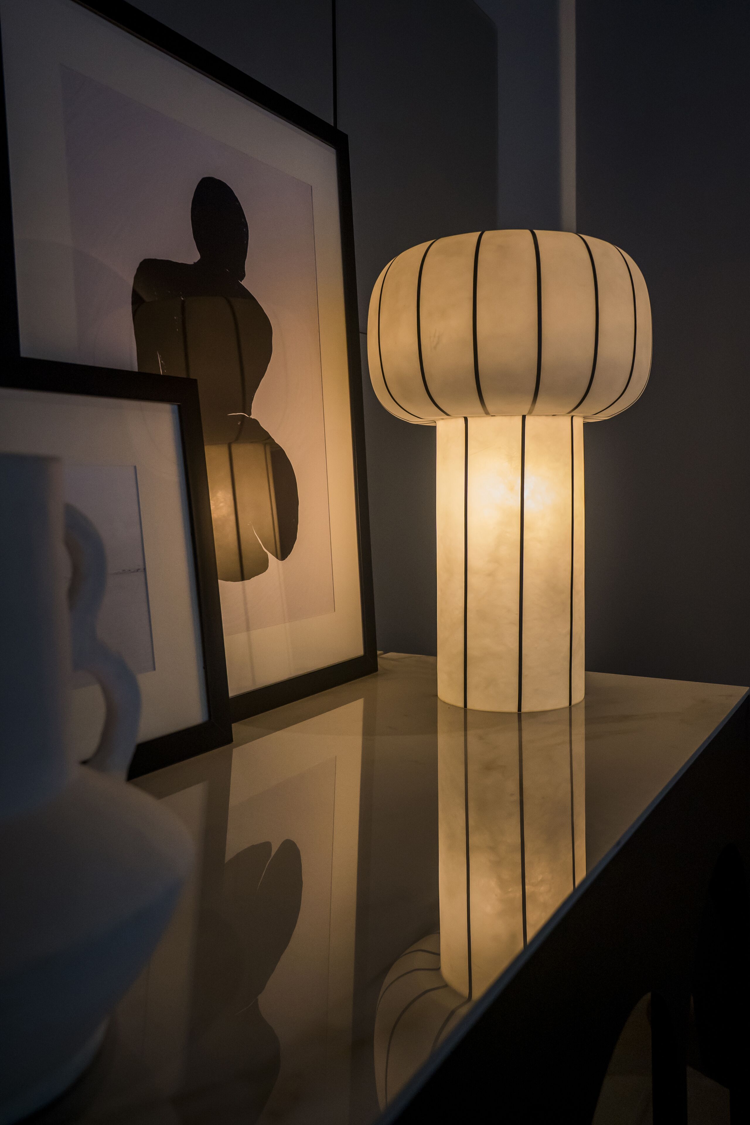A modern interior with a reflective surface, a cylindrical light fixture, and framed artwork.