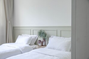 Une chambre d’hôtel avec deux lits simples, du linge de lit blanc, une table de chevet avec deux vases et une plante en pot.