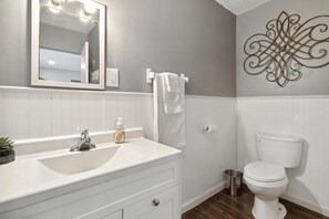 Une salle de bain avec un meuble-lavabo blanc, un miroir, un évier, des toilettes et un élément décoratif mural.