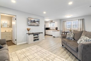 A modern living room with a grey sofa, a coffee table, and a patterned rug. - The Pinny City Suite (Pinconning)