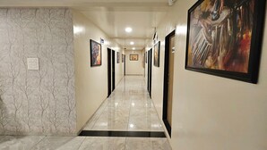A hallway with marble flooring, framed artwork on the walls, and doors leading to rooms. - Annapurna Executive (Tuljapur)