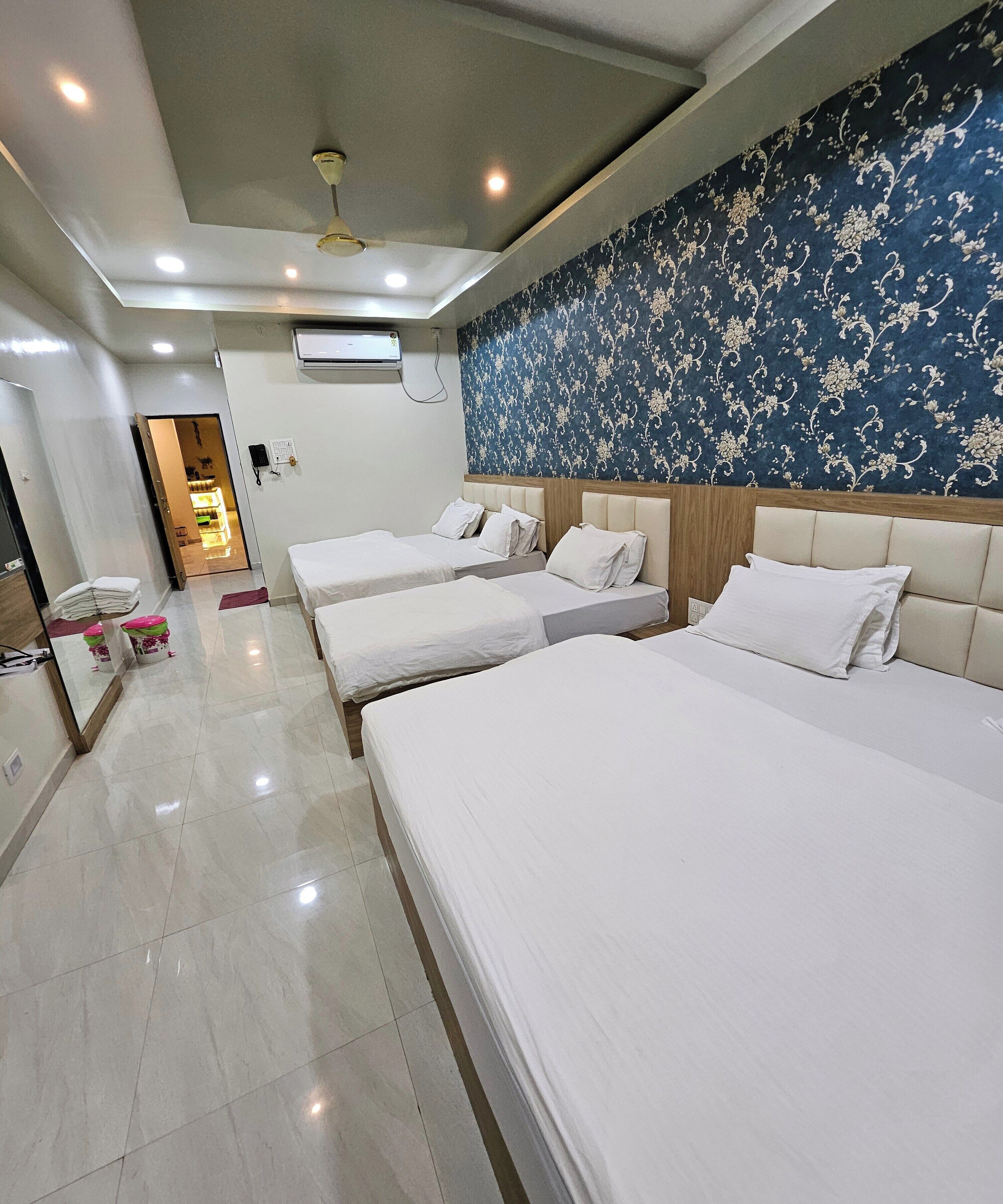 A hotel room with three single beds, a large mirror, a ceiling fan, and a patterned wall.
