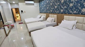 A hotel room with three single beds, a large mirror, a ceiling fan, and a patterned wall.