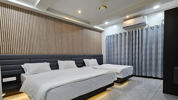 A modern bedroom with a large bed, a wooden panel wall, and an air conditioning unit. - Annapurna Executive (Tuljapur)