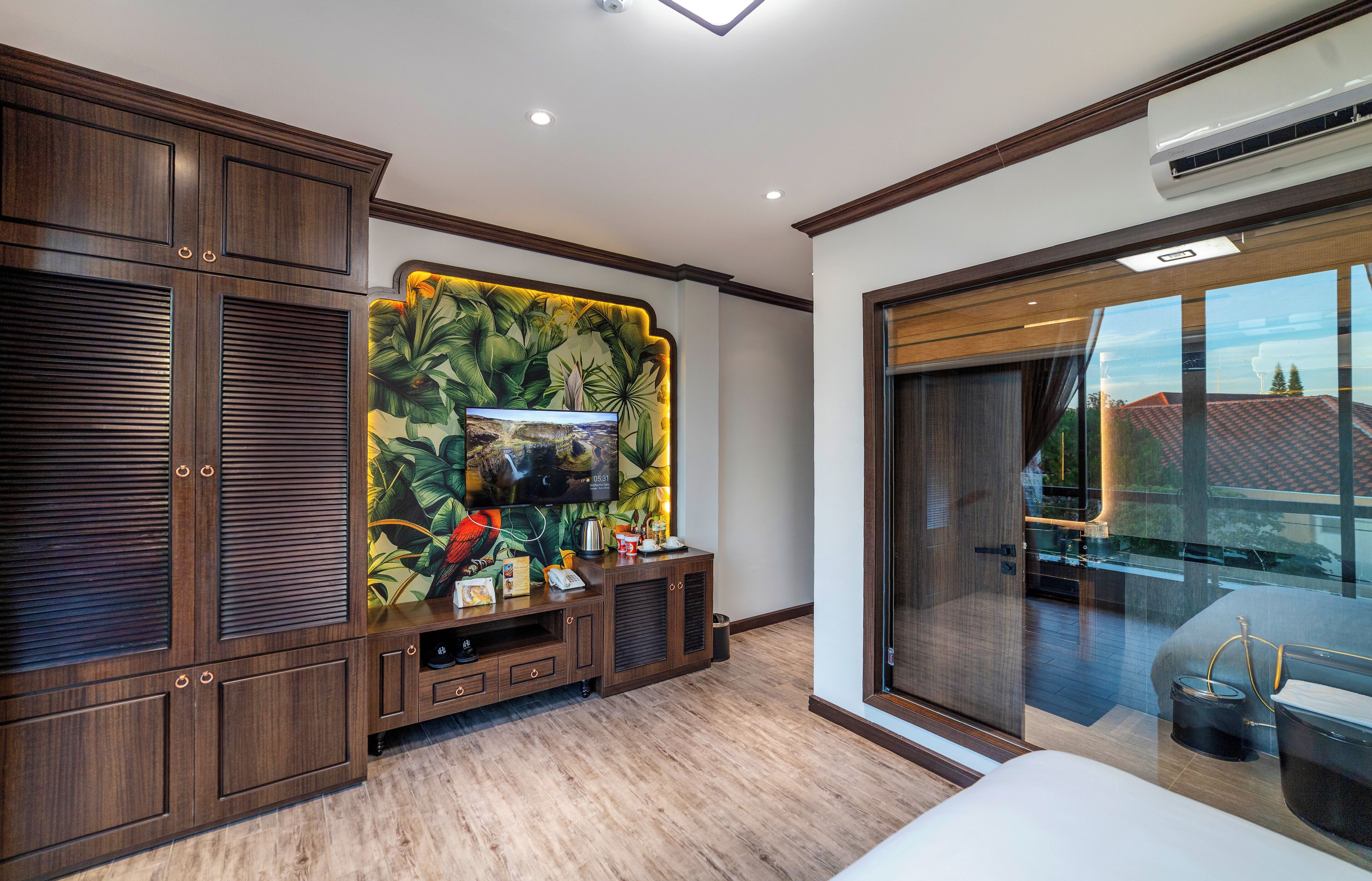 A modern bedroom with a large TV, wooden cabinets, and a balcony with a view.