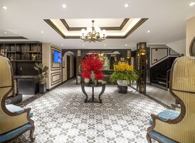 A spacious lobby with a high ceiling, a chandelier, a central table with floral arrangements, and a television mounted on the wall.