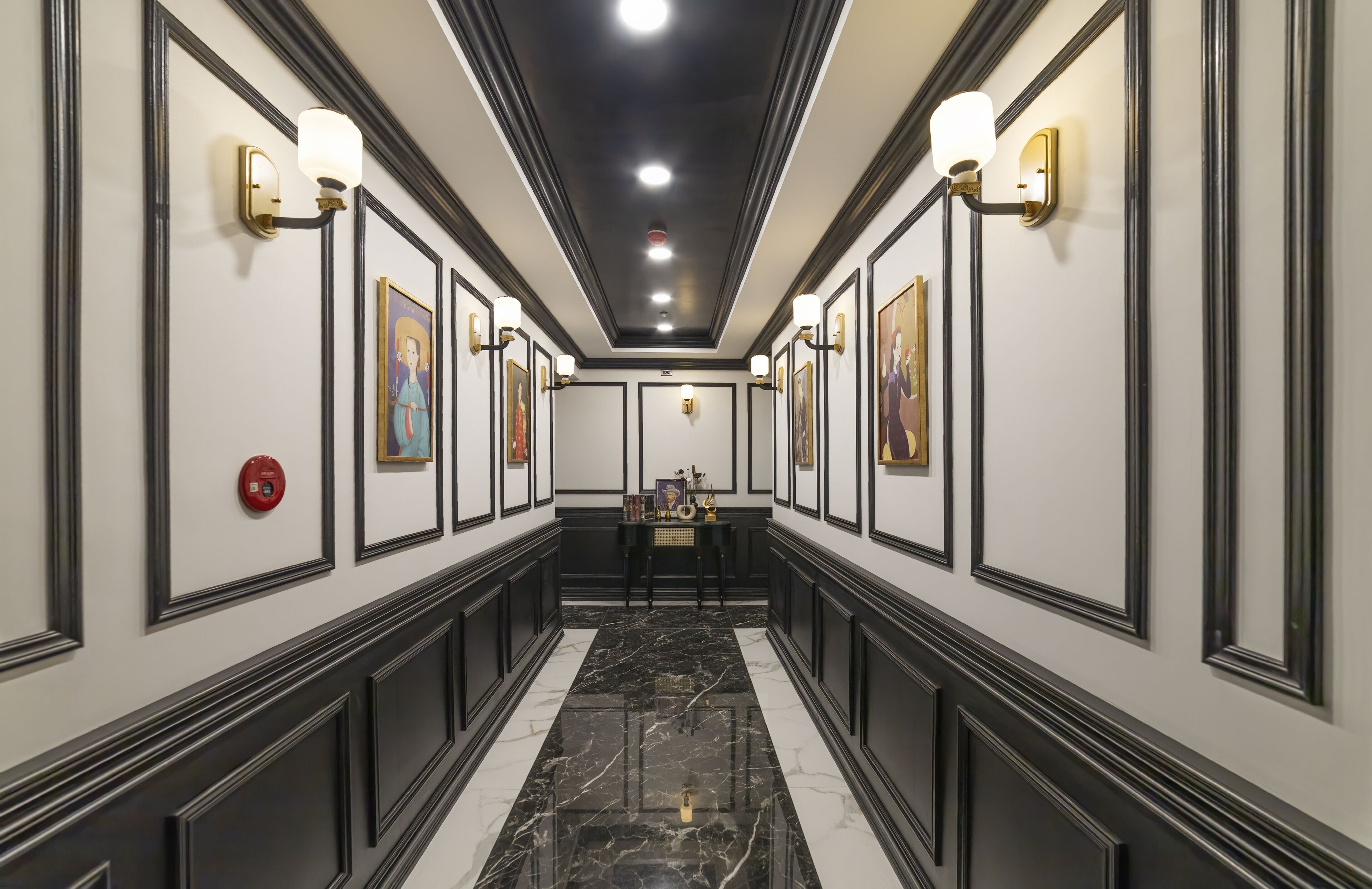 A hallway with framed artwork on the walls, a marble floor, and wall-mounted light fixtures.
