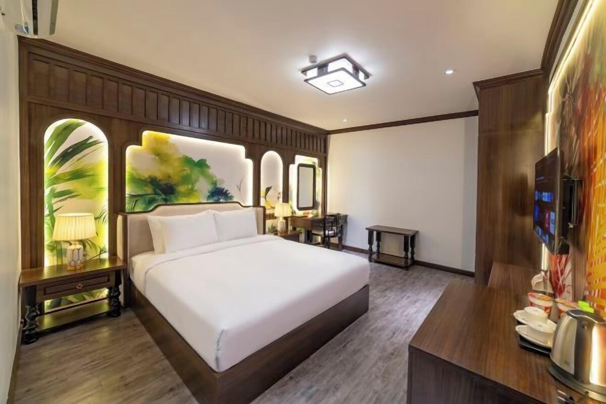 A hotel room with a large bed, a desk, a mirror, and a television.