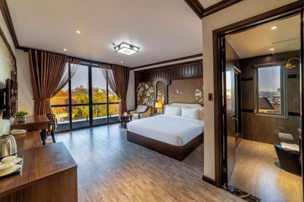 A spacious bedroom with a large bed, a desk with a chair, and a view of the city through large windows.