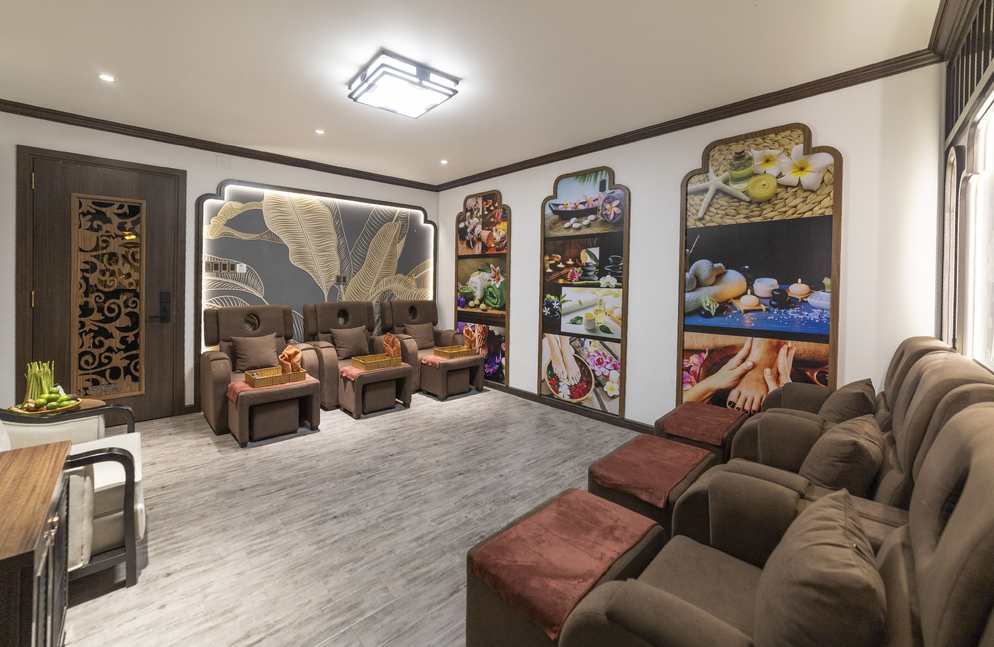 A modern spa room with massage chairs, a wooden decorative panel, and wall art depicting various spa-related themes.