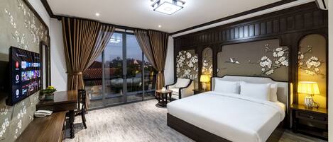 A modern hotel room with a large bed, a TV on the wall, a dining area, and a view of the outside.