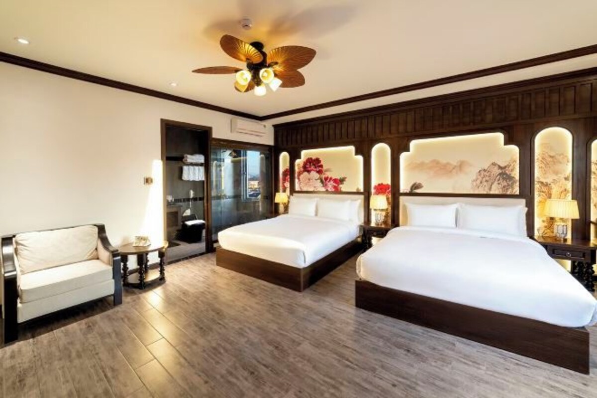 A hotel room with two beds, a sofa, a ceiling fan, and decorative wall panels.