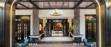 A lobby with a stone wall, a chandelier, and two black doors.