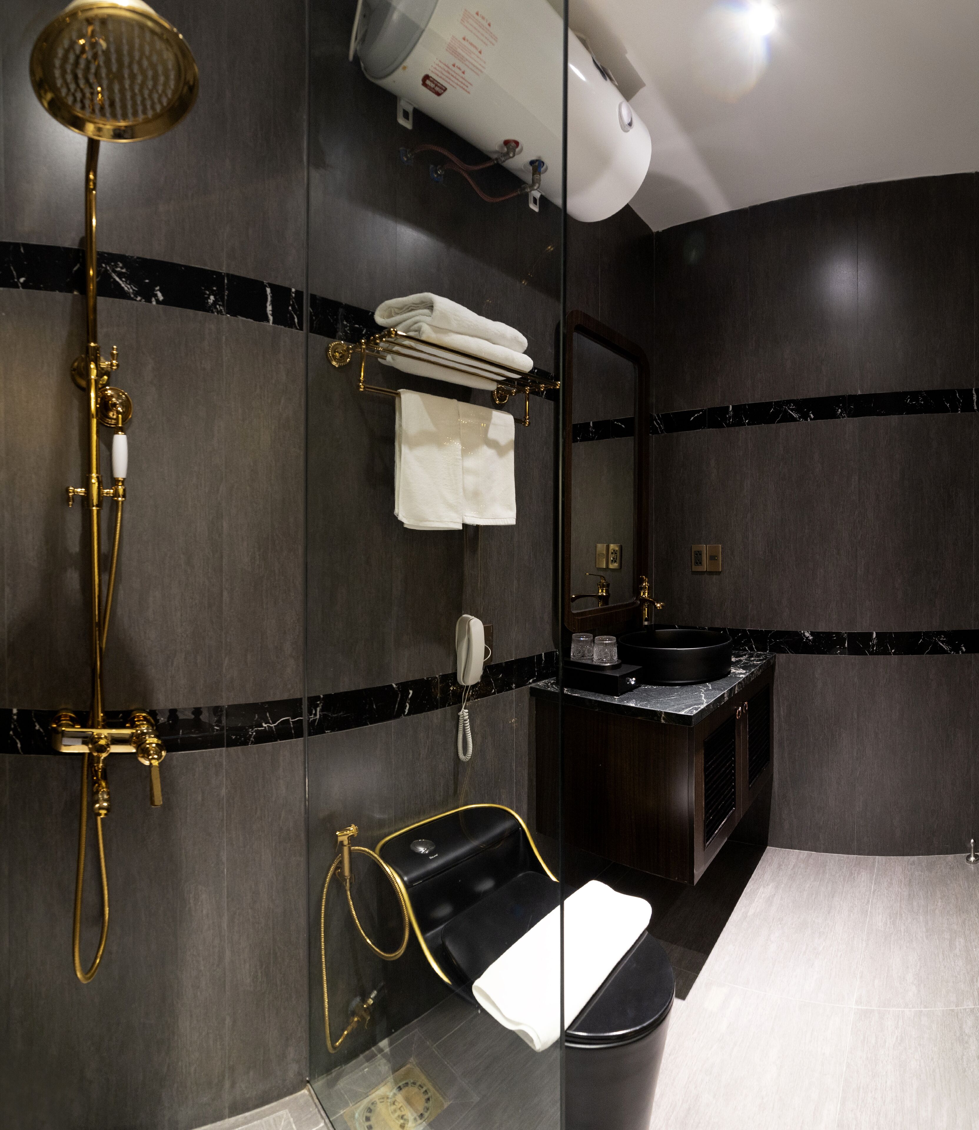Un baño moderno con ducha envuelta en vidrio, lavamanos de mármol negro y un espejo grande.
