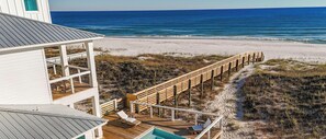 Une maison de plage avec une terrasse en bois, une piscine et une vue sur l’océan.