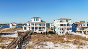 A beachfront property with multiple buildings, including a large two-story house with a balcony and a smaller adjacent structure. - Lavish Beach Sanctuary with Private Pool and Boardwalk | Sugar Shores by Kaiser Vacation Rentals (Gulf Shores)
