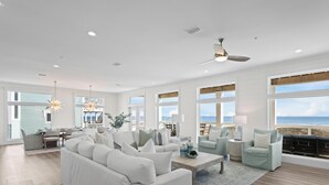 A spacious living room with a white sofa, a coffee table, and a fireplace. There are large windows with a view of the ocean. - Lavish Beach Sanctuary with Private Pool and Boardwalk | Sugar Shores by Kaiser Vacation Rentals (Gulf Shores)