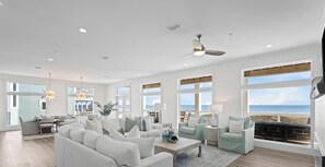 Un salon spacieux doté d’une grande fenêtre donnant sur la plage, d’un ventilateur de plafond et d’un coin repas avec vue.