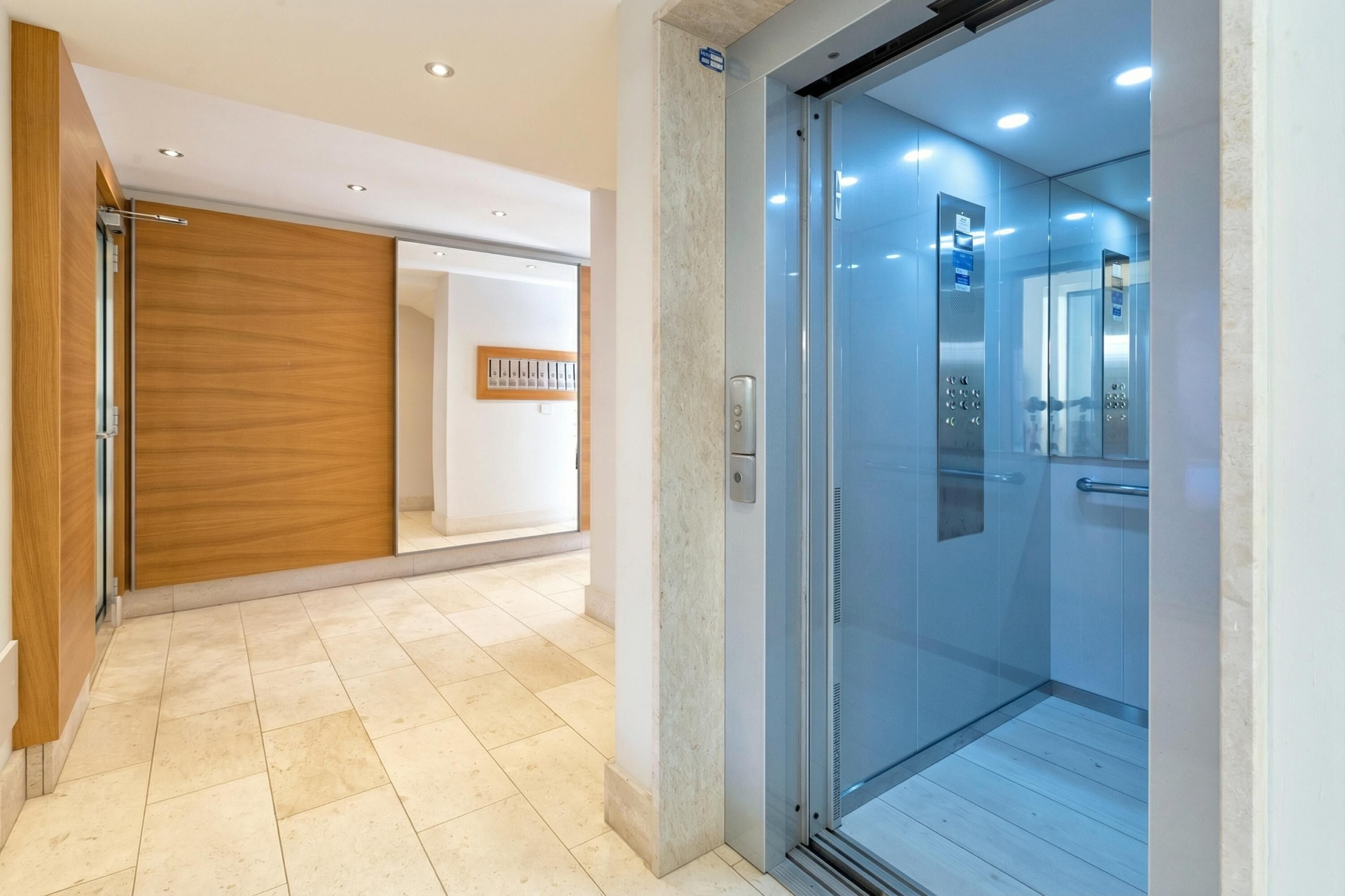 Een moderne lift met glazen deuren, een wand van houtfineer en een betegelde vloer.