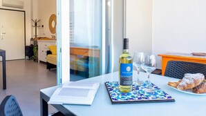 A modern living room with a dining area, a sofa, a table with a bottle of alcohol, glasses, and a plate of food. - Bilocale Vista Mare Giorgio (Alghero)