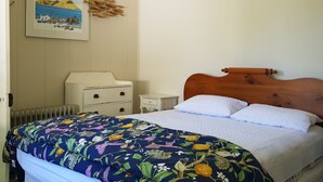 A bedroom with a wooden headboard, a floral bedspread, a white bedside table, a white dresser, and a framed picture on the wall. - Peaceful and private bach just a few minutes walk to village centre and pools (Hanmer Springs)