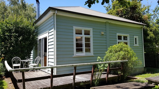 A small, light green wooden house with a porch, a chimney, and a small garden area with a picnic table. - Peaceful and private bach just a few minutes walk to village centre and pools (Hanmer Springs)
