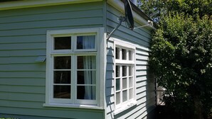A light green building with a chimney, a satellite dish, and a window with curtains. - Peaceful and private bach just a few minutes walk to village centre and pools (Hanmer Springs)