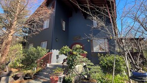 Uma casa de dois andares com fachada escura, telhado vermelho e entrada frontal com degraus até a porta.