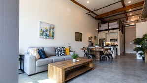 Un salon moderne avec un canapé gris, une table basse en bois et un coin repas comprenant des chaises, avec une cuisine en arrière-plan.