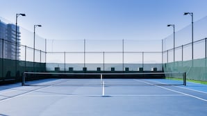 Una cancha de tenis interior con red, rodeada de paredes y mallas, y farolas.