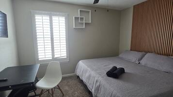 Ein Schlafzimmer mit Bett, Schreibtisch, Stuhl, Deckenventilator und Fenster mit Jalousien.