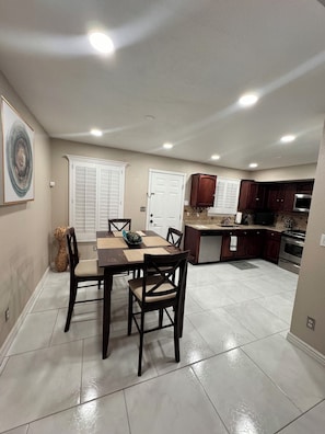 A dining area with a table and chairs, a kitchen with cabinets and appliances, and a door with a window.