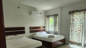 A hotel room with two beds, a window with curtains, an air conditioning unit, and a tiled floor.