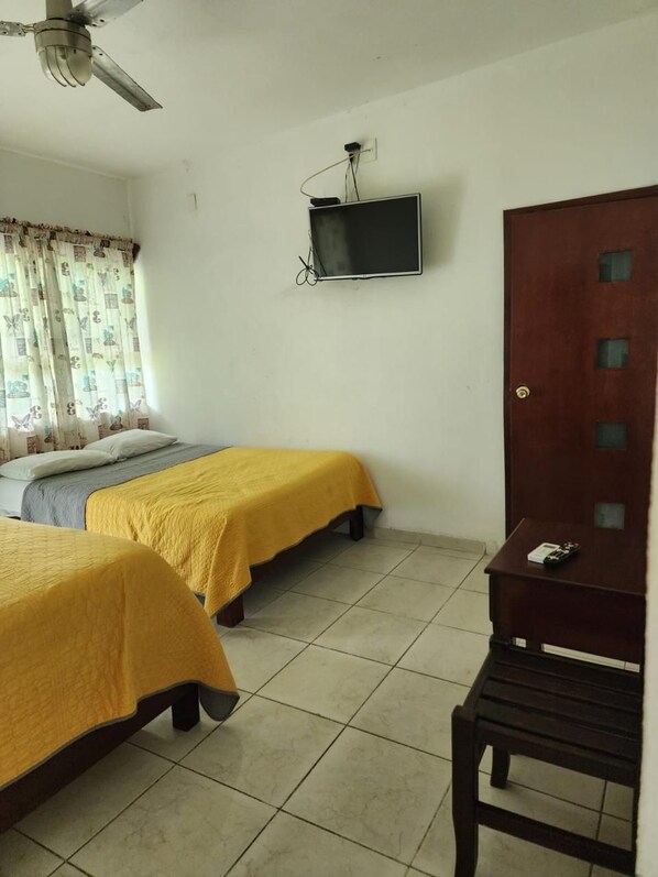 Una habitación con dos camas, un televisor fijado a la pared y un armario de madera.