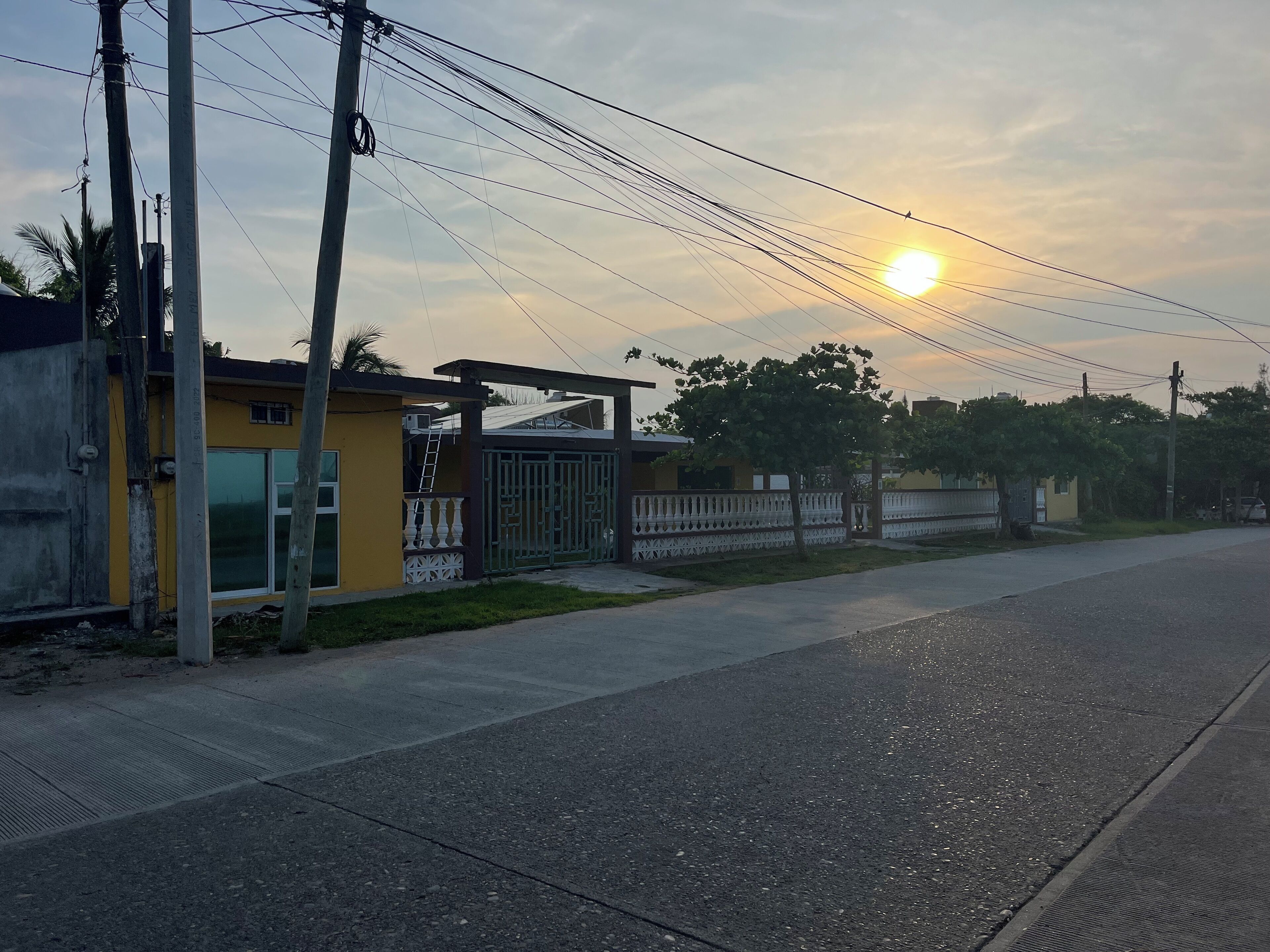 A residential street with a yellow house, a gated area, and utility poles.