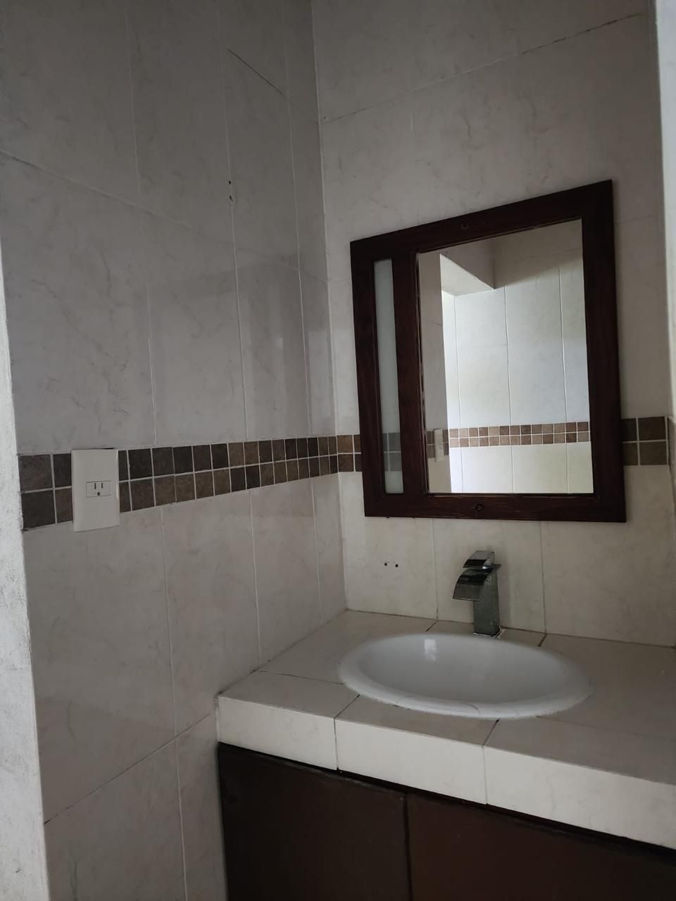 A bathroom with a white sink, a mirror with a dark frame, and a tiled backsplash.