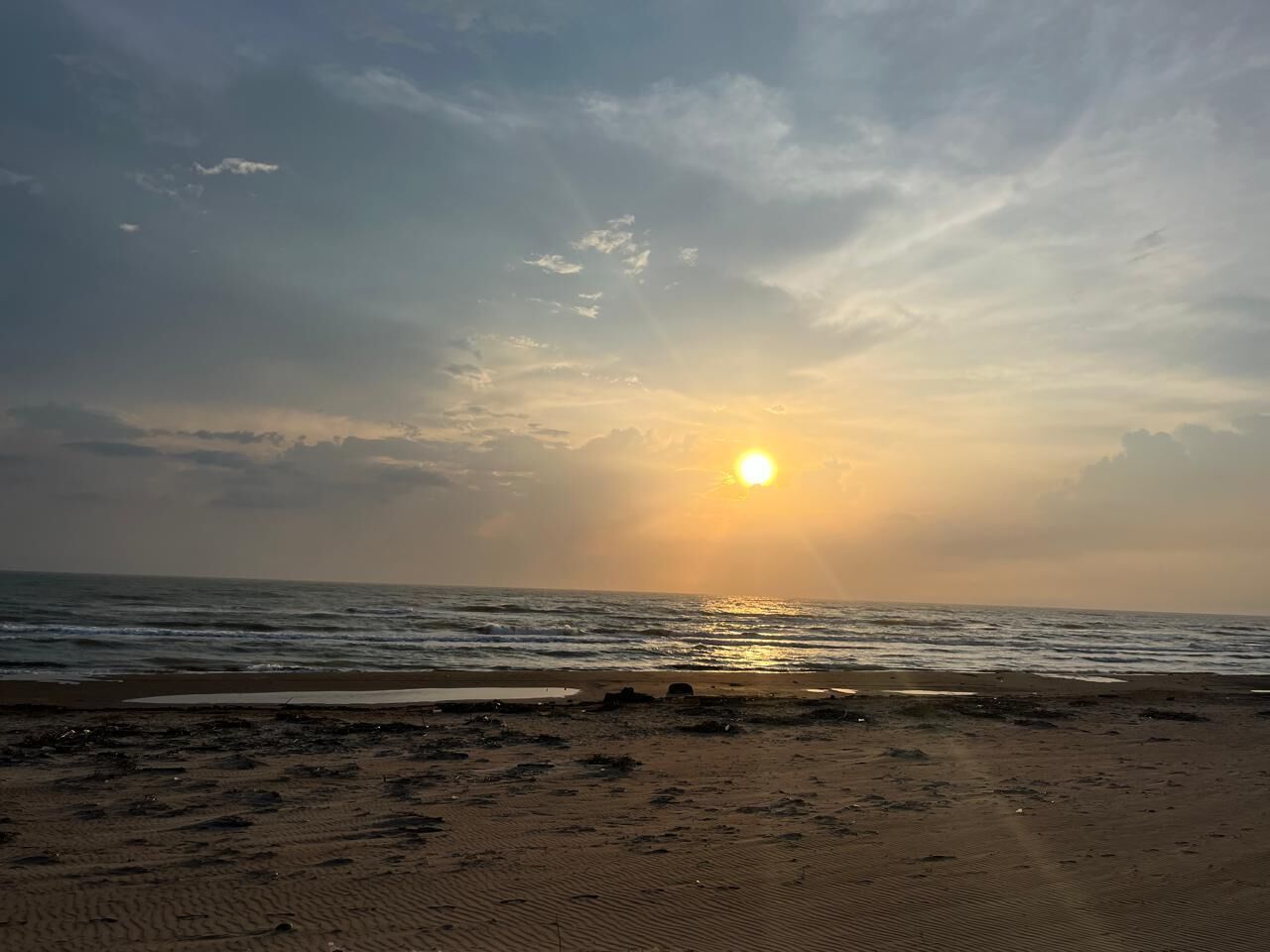 Una playa con el sol poniéndose en el horizonte.