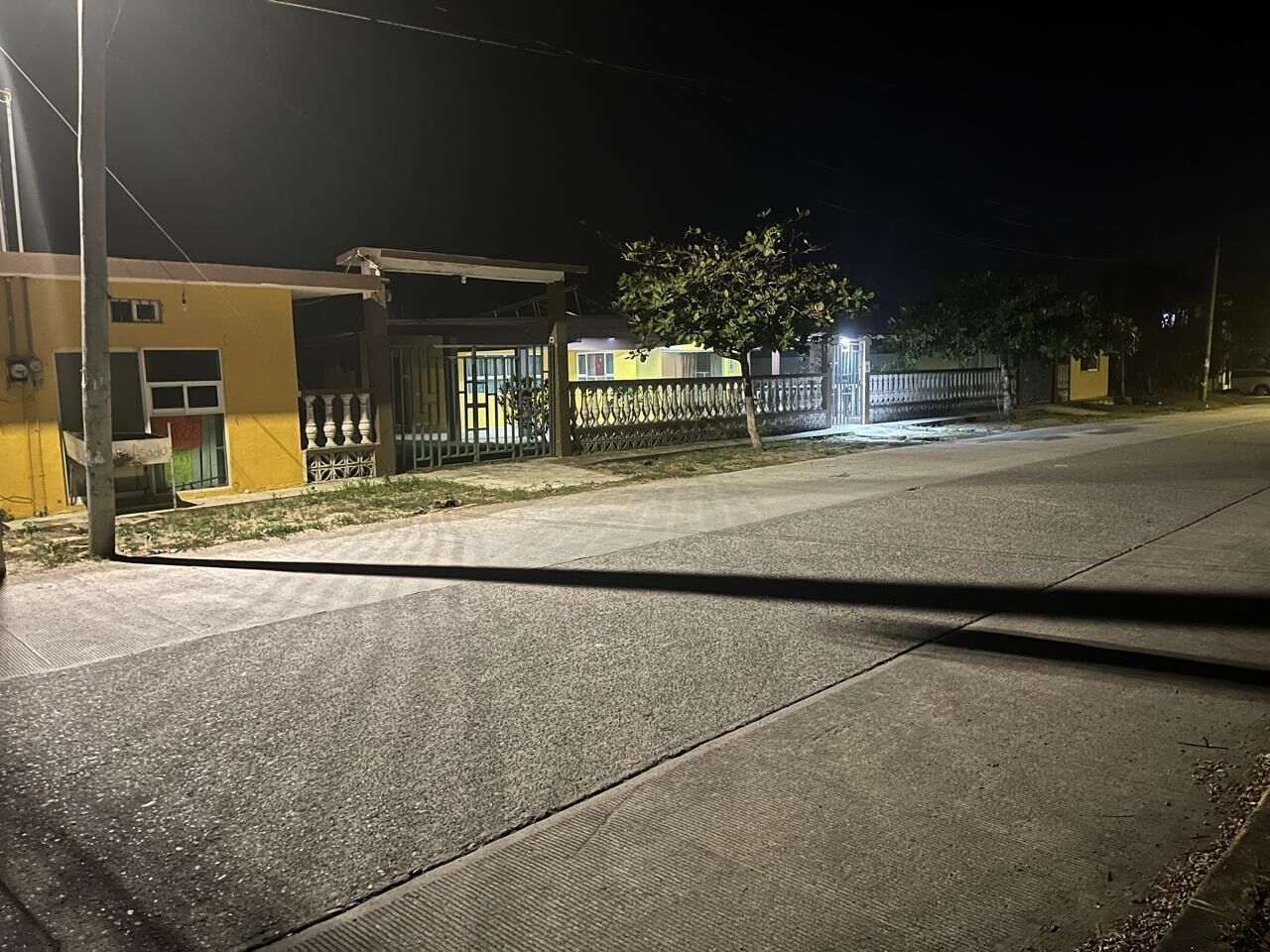 Una calle iluminada de noche, con un edificio que tiene una entrada protegida por una reja y un pequeño estacionamiento.