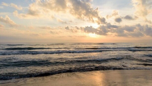 A beach with waves and a sunset.